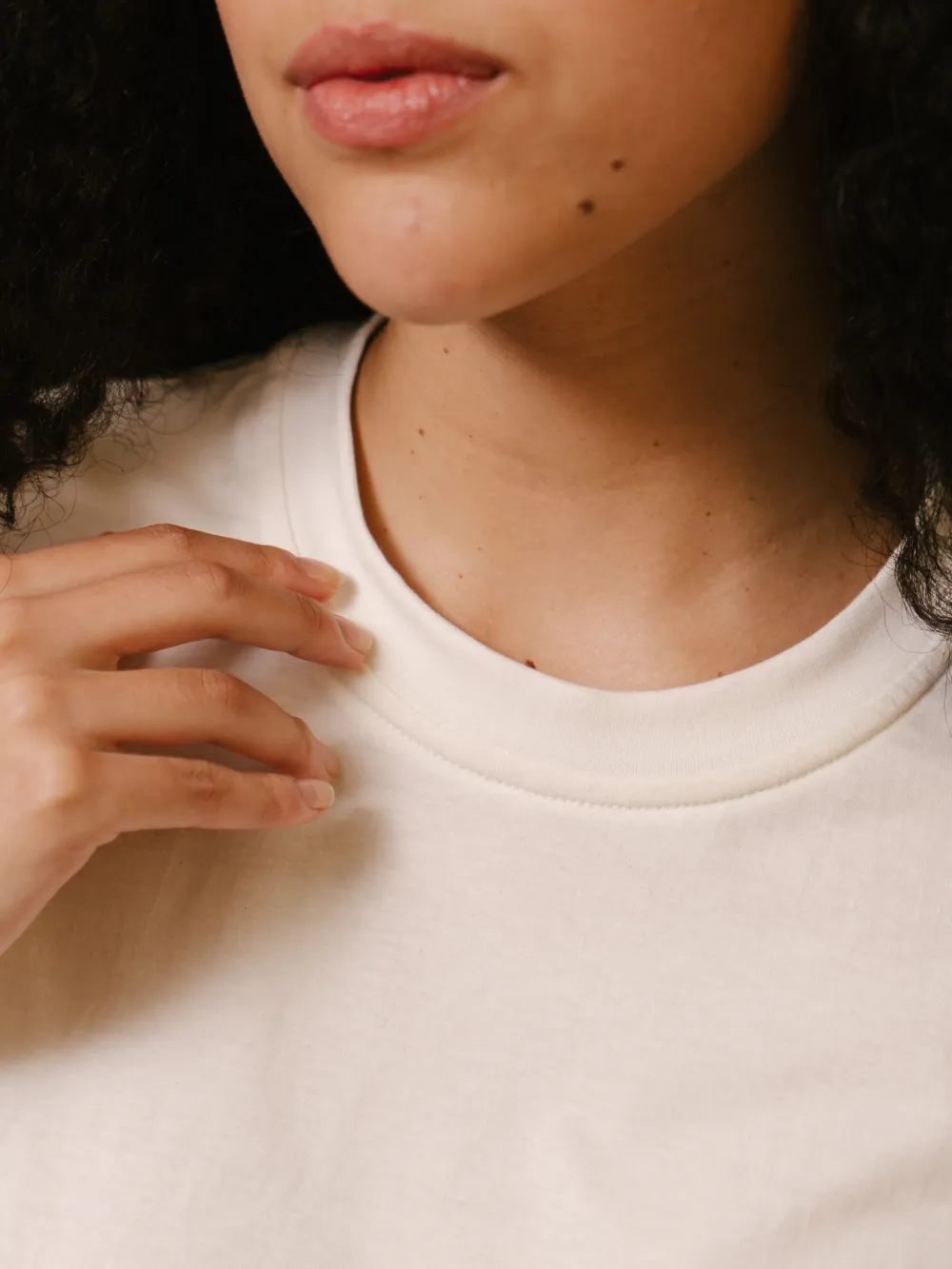 Close do decote da camiseta off-white, com a gola fechada e nenhuma etiqueta na nuca.